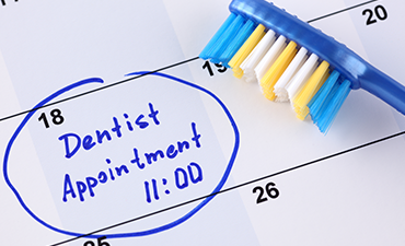 The image features a calendar page with a highlighted dentist appointment time, a blue toothbrush lying on top of the calendar, and a handwritten note above the highlighted time that reads dentist appointment in black marker.
